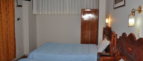 A hotel room with two beds, a television mounted on the wall, a wooden headboard, and a nightstand with a lamp.