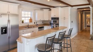 A modern kitchen with white cabinetry, a stainless steel refrigerator, an oven, and a built-in island with bar stools. - Screne Cabin, Dock, Beach, HotTub, FirePit, Kayak (Goodview)