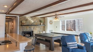 A spacious living area with a stone fireplace, a ping pong table, and a large window offering a view of the outdoors. - Screne Cabin, Dock, Beach, HotTub, FirePit, Kayak (Goodview)
