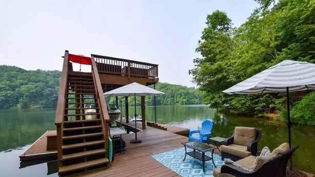 A wooden deck with a staircase leading to a balcony, outdoor furniture, and umbrellas. - Screne Cabin, Dock, Beach, HotTub, FirePit, Kayak (Goodview)