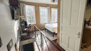 Un dormitorio con cama, dos ventanas, una puerta y una escalera.