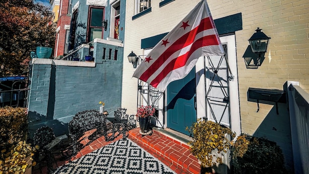 Un edificio con fachada azul y blanca, una bandera y un vestíbulo con baldosas estampadas.
