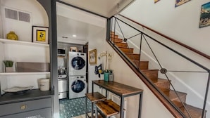 Una cocina compacta con lavadora y secadora integradas, una pequeña mesa de comedor y una escalera que sube a un nivel superior.