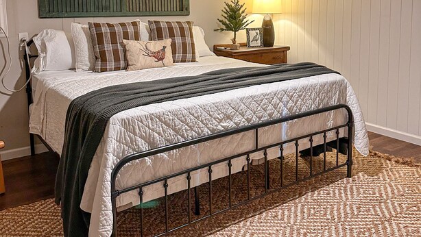 A bedroom with a bed, a ceiling fan, a nightstand with a lamp, and a wall-mounted headboard.