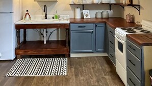 A compact kitchen with a sink, stove, and cabinets. There are hanging lights and a patterned rug on the floor.