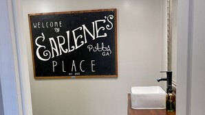A bathroom with a blackboard sign reading "Welcome to Earlene's Place" and a green sink.