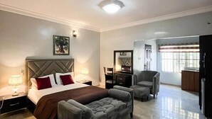 Un dormitorio moderno con una cama grande, un sofá gris y un sillón pequeño. Hay un escritorio y una silla en la esquina.