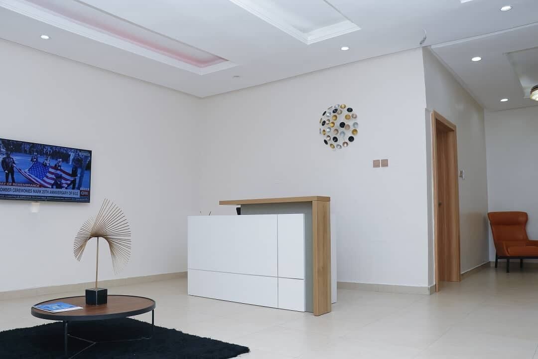 Un moderno vestíbulo de hotel con un diseño minimalista, que presenta un televisor de pantalla plana grande, una pieza de arte mural original y una zona de estar con una silla.