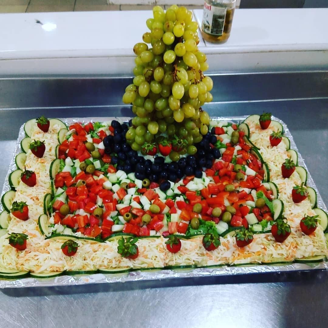 Un plateau de nourriture disposé de manière décorative, comprenant des raisins, des tomates, des concombres et du fromage.