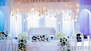Decoración para una ceremonia de boda con un altar blanco, arreglos florales e iluminación colgante.