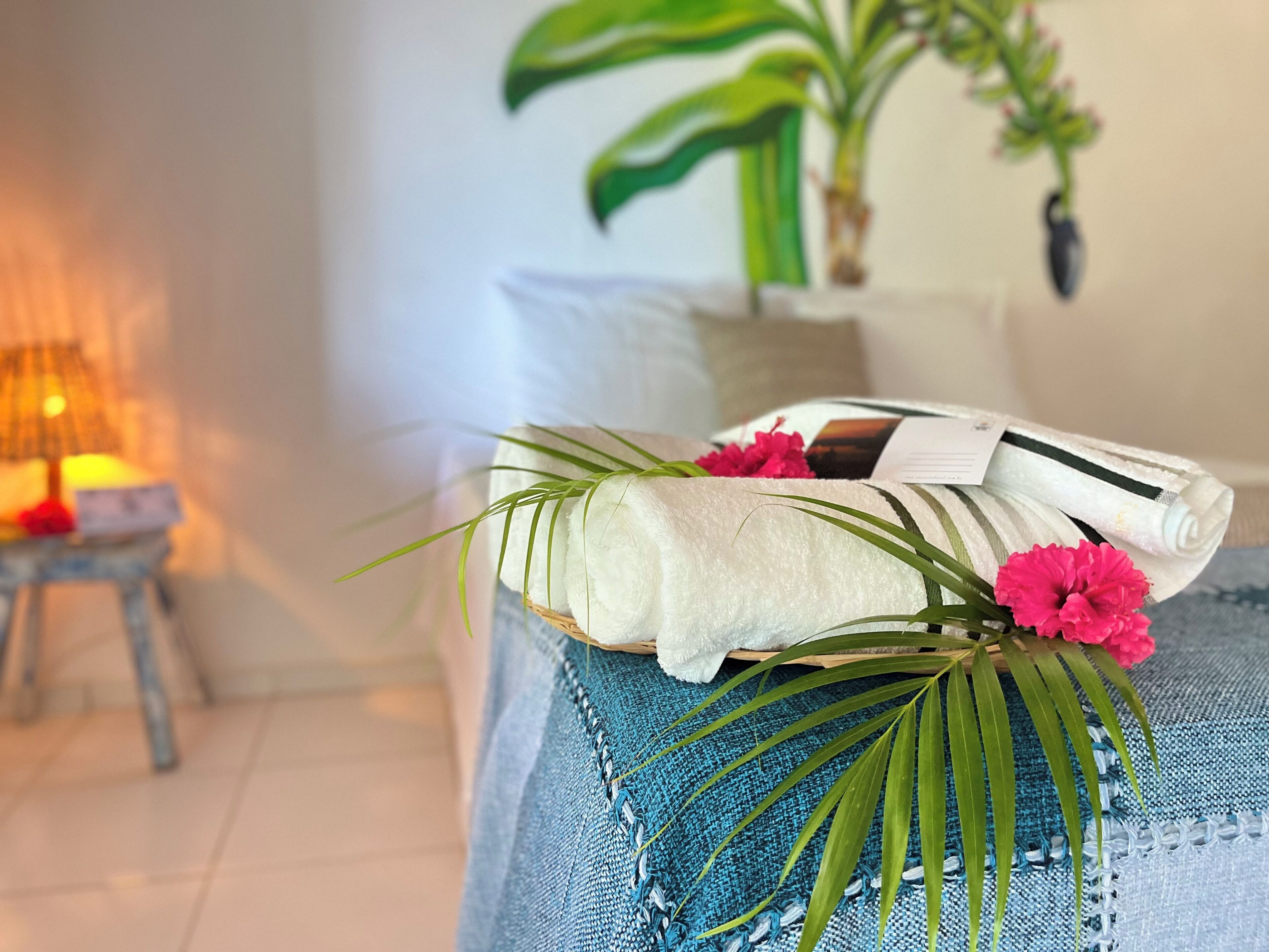 A neatly arranged room with a bed, a small table with a lamp, and a potted plant.