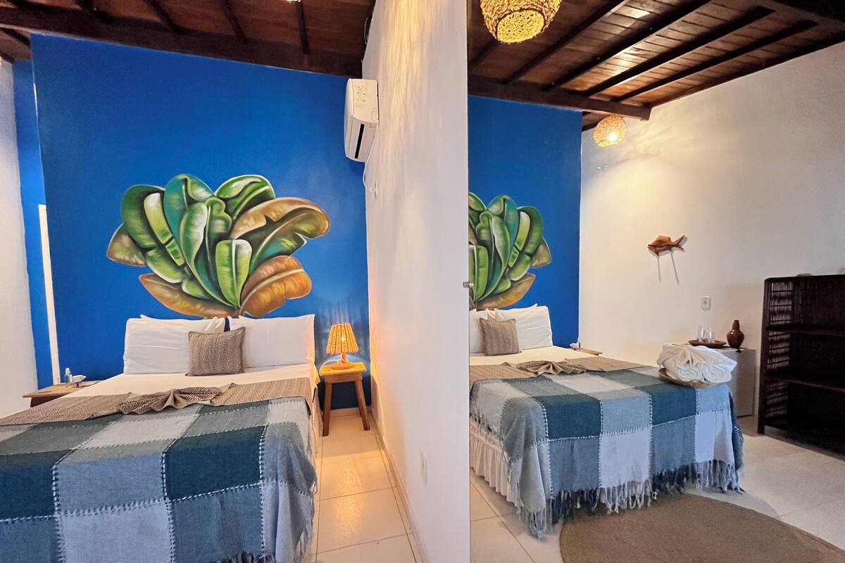 A room with two beds, a blue wall mural, a wooden ceiling, and a small table with a lamp.