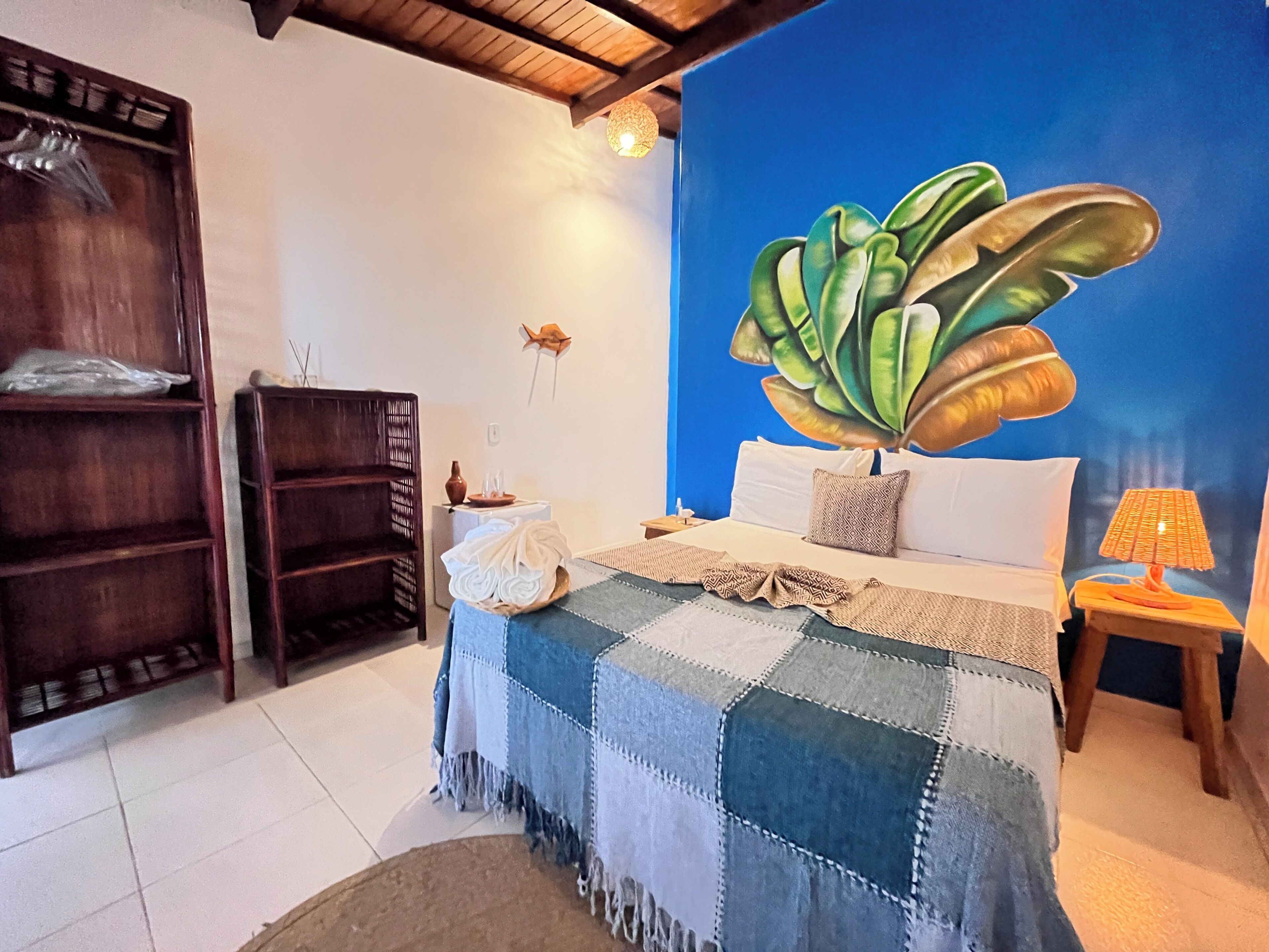 Un dormitorio con cama, mesita de noche, estante en la pared y un cuadro de una planta grande.