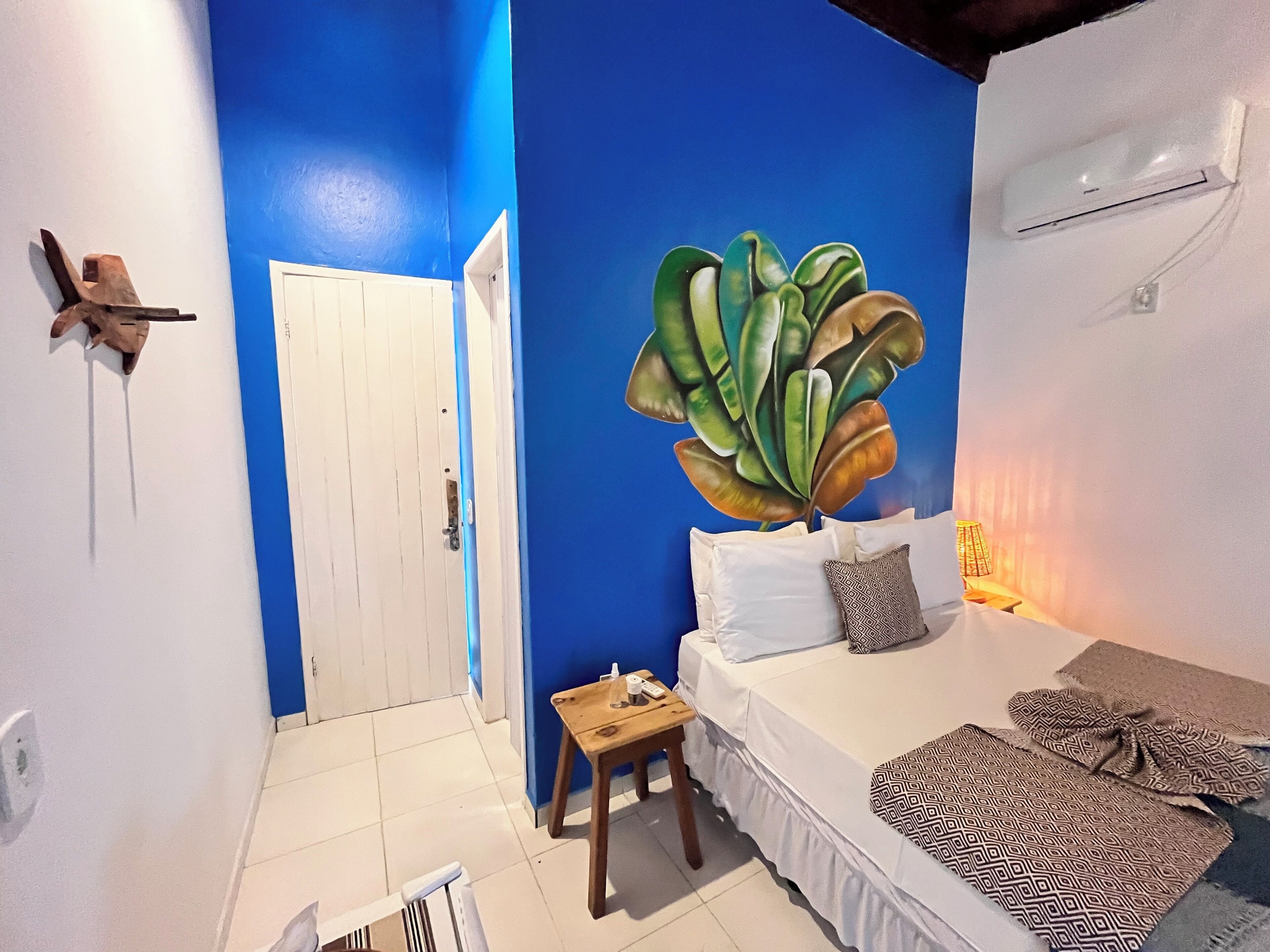 A room with a blue accent wall, a bed with white bedding, a small wooden table, and a large plant.