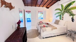 A bedroom with a bed, a small table, a potted plant, and a window with a view of a bridge. - Pousada Nascente do Sol (Cairu)