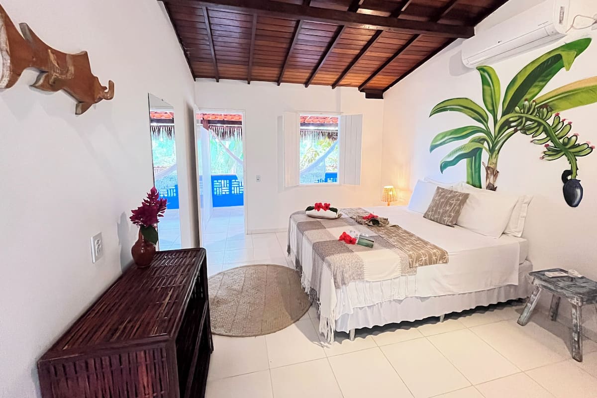A bedroom with a bed, a small table, a potted plant, and a window with a view of a bridge.