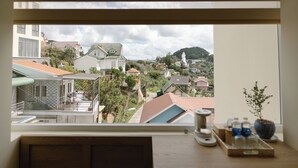A view from a window overlooking a residential area with various buildings, a statue, and a hill in the distance. - The Gardener by WeDalat (Xuan Huong - Da Lat)