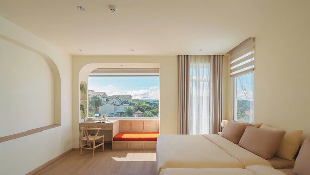 A hotel room with a bed, a desk, a chair, and a view of the cityscape. - The Gardener by WeDalat (Xuan Huong - Da Lat)