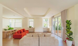 Ein geräumiges Wohnzimmer mit einer großen Couch, einer kleineren Couch und einem Essbereich mit Tisch und Stühlen. Mehrere Fenster sorgen für natürliches Licht und Ausblick ins Freie.