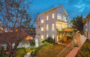 Ein modernes, zweistöckiges Haus mit einem gepflegten Garten, einem Balkon und einer Treppe, die zum Eingang führt.