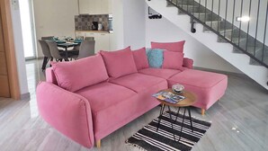 Una sala moderna con un sofá seccional rosa, una pequeña mesa redonda y una escalera con barandilla de metal.