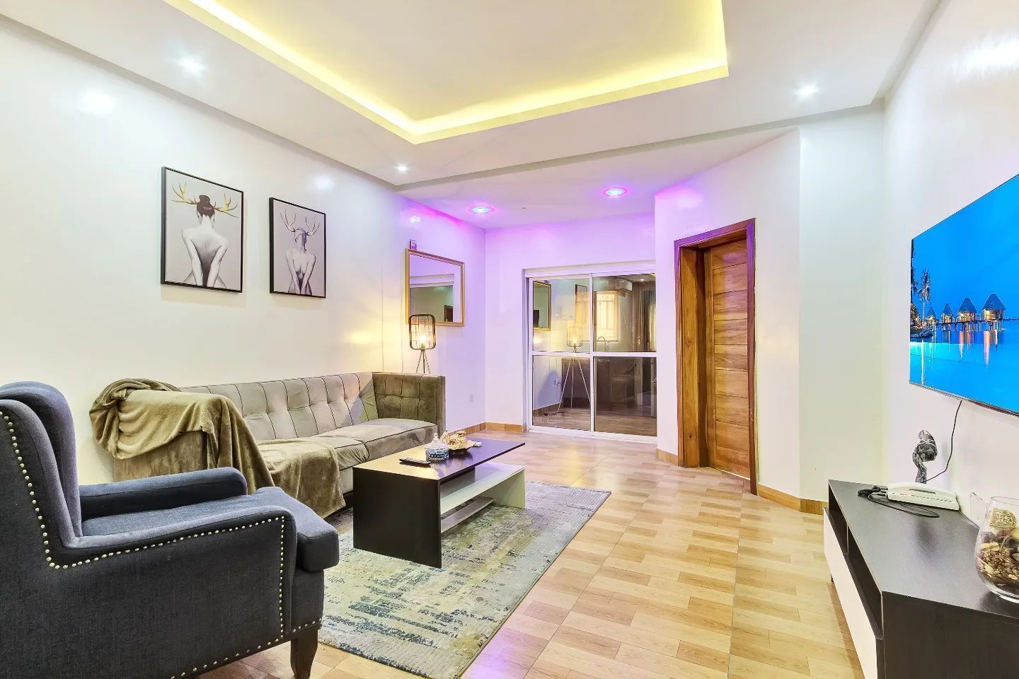 Een moderne woonkamer met een bank, salontafel en een televisie. Er is een schuifdeur die leidt naar een balkon.