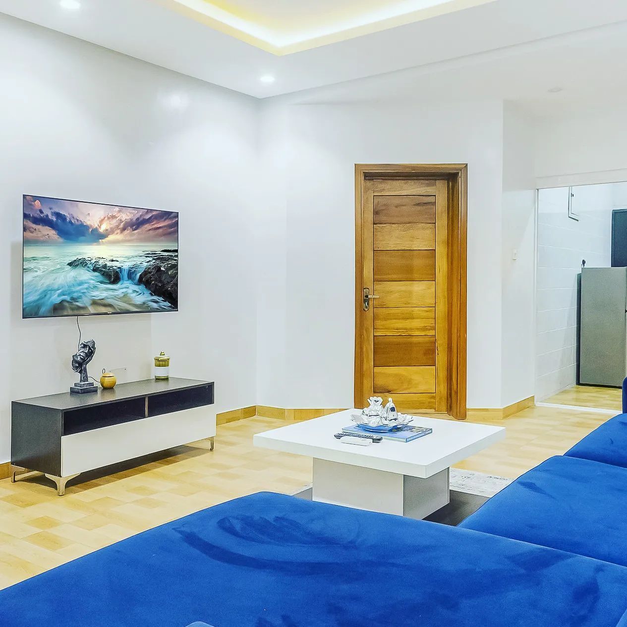 A living room with a TV, a wooden door, a white table, and blue sofas.