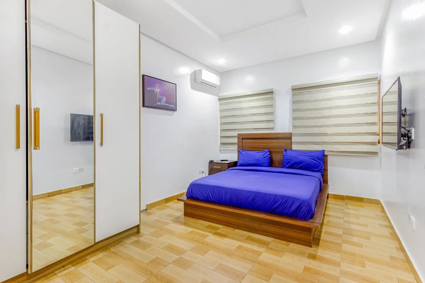 Un dormitorio con cama, armario, mesita de noche y televisor montado en la pared.
