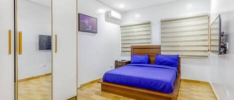 Un dormitorio con cama, armario, mesita de noche y televisor montado en la pared.