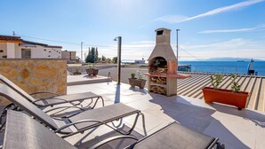 Eine Dachterrasse mit Sitzgelegenheiten im Freien, einem Holzofen und Blick aufs Meer.