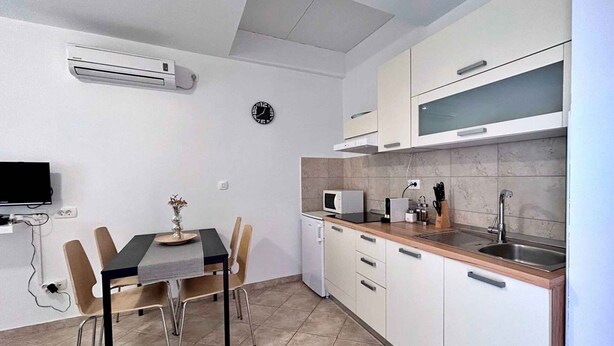 A compact kitchen with a dining table, chairs, a microwave, and a sink. - Holiday apartment with sea view and barbecue facilities (Čižići)