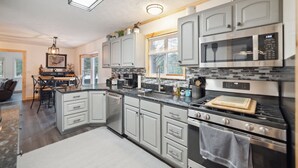 Una cocina moderna con gabinetes grises, horno empotrado, microondas y una zona de comedor con mesa y sillas de madera.