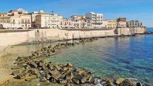 A coastal town with buildings along the waterfront, clear blue water, and rocky shoreline. - Vacation home Fanusa by Interhome (Siracusa)