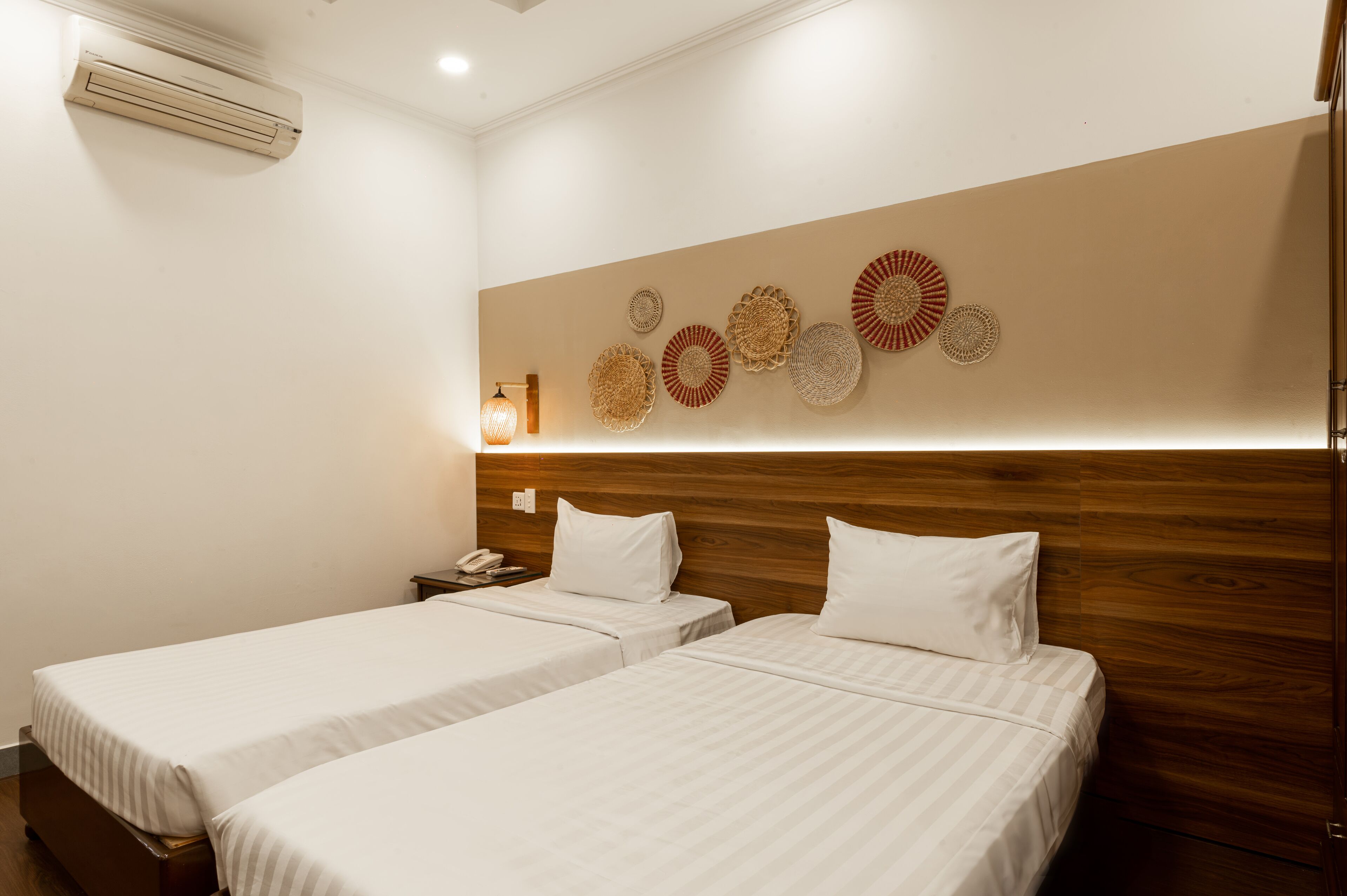 A hotel room with two single beds, a wooden headboard, a wall-mounted air conditioner, and decorative wall art.