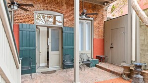 A brick building with a covered patio area featuring a door, two chairs, a table, and a decorative urn.