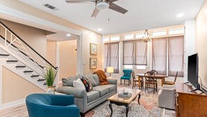 A modern living room with a grey sofa, blue armchairs, a coffee table, and a dining area with a chandelier.