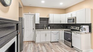 A modern kitchen with white cabinets, a black herringbone backsplash, a microwave, stove, dishwasher, and a clock on the wall.