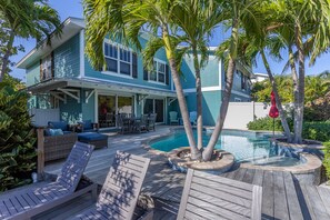 Relax on the spacious deck with a swimming pool, lounge chairs, and dining table, surrounded by lush tropical landscaping.