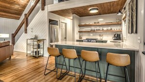 A modern kitchen with a central island, bar stools, and a wooden staircase. - Sunrise and Stardust - Hot Tub | Mountain Views | Screened Porch | (Morganton)