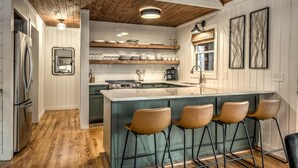 A modern kitchen with a central island, bar stools, and wooden flooring. - Sunrise and Stardust - Hot Tub | Mountain Views | Screened Porch | (Morganton)