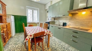 A kitchen with a dining table, chairs, a refrigerator, cabinets, and a window.