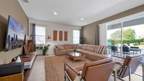 A spacious living room with a large sofa set, a coffee table, and a TV. There is a dining area with a table and chairs visible through a glass door. - Modern Oasis. Enjoy Resort amenities, 10 min to Disney and Attractions.  (Kissimmee)