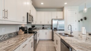 A modern kitchen with white cabinets, a stainless steel refrigerator, a double sink, and a marble countertop. - Modern Oasis. Enjoy Resort amenities, 10 min to Disney and Attractions.  (Kissimmee)