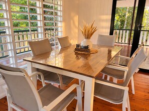 Un comedor con una mesa de madera y sillas blancas, un letrero de bienvenida y un jarrón con plantas secas.