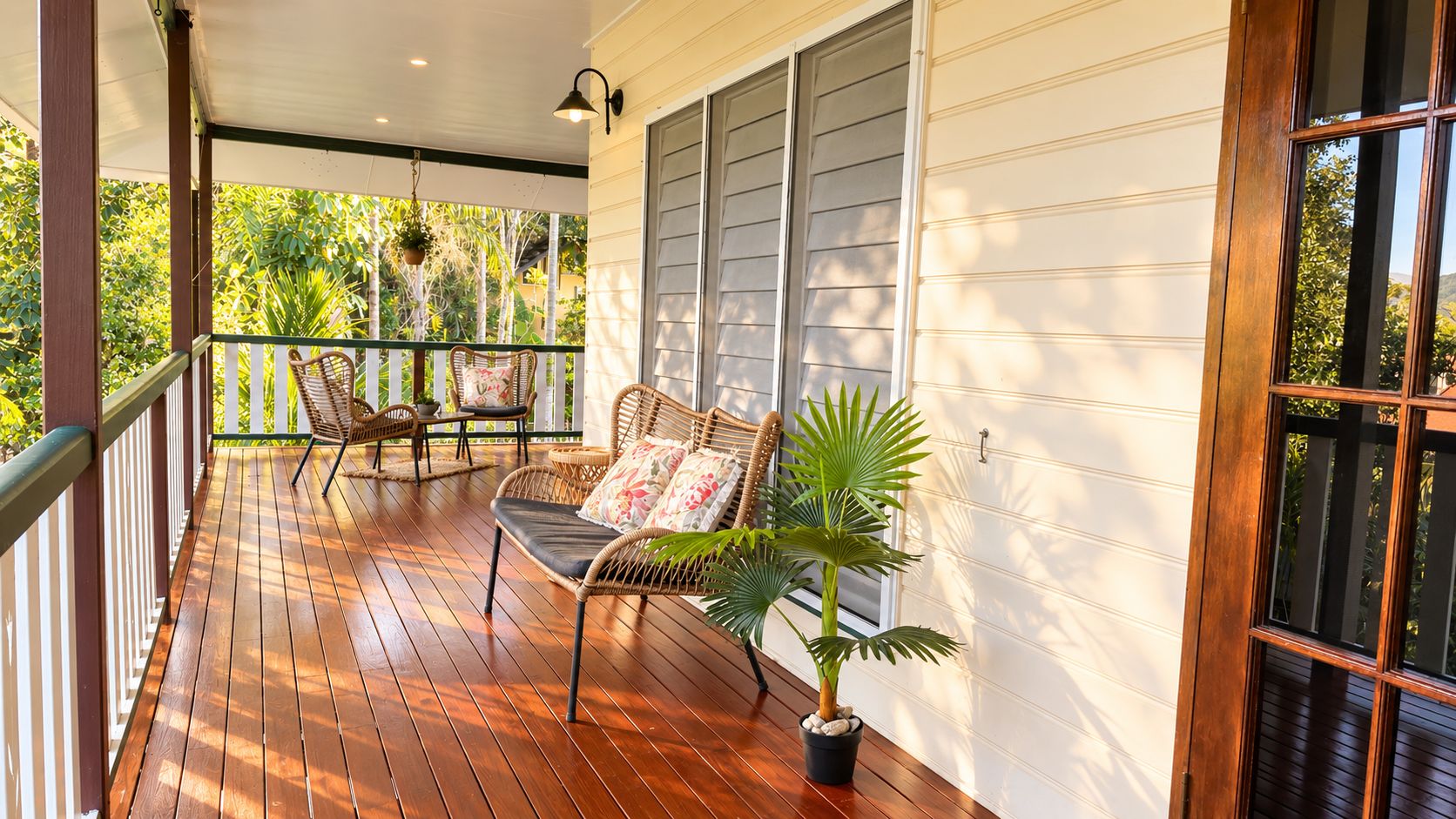 A wooden porch with a bench and chairs, a potted plant, and a window with blinds.