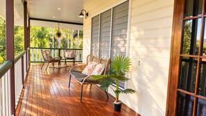 Une véranda en bois avec un banc et des chaises, une plante en pot et une fenêtre avec des stores.