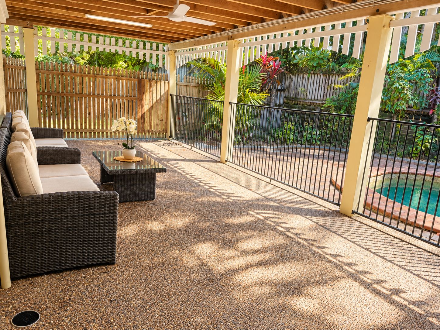 Un patio couvert avec des meubles d’extérieur, une piscine et une clôture en bois.