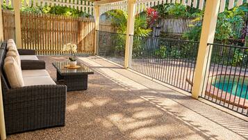 Un patio couvert avec des meubles d’extérieur, une piscine et une clôture en bois.