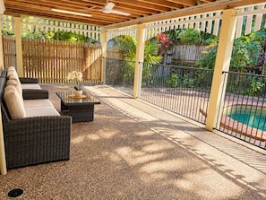 Ein überdachter Patio-Bereich mit Gartenmöbeln, einem Pool und einem Holzzaun.