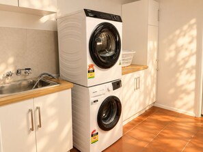Un espace buanderie compact comprenant une machine à laver et un sèche-linge superposés, un évier et un plan de travail en bois.